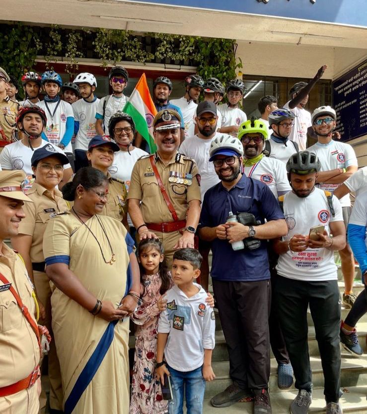 The image shows a group of people, including police officers, cyclists, and children, gathered together for a community event. Some participants are wearing helmets and Cycle Wala T-shirts, indicating a cycling-themed event, likely organized by or associated with the brand Cycle Wala.